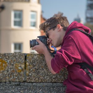 Young photographer in a burgundy hoodie looks through the viewfinder along the stone wall of the Hotwalls