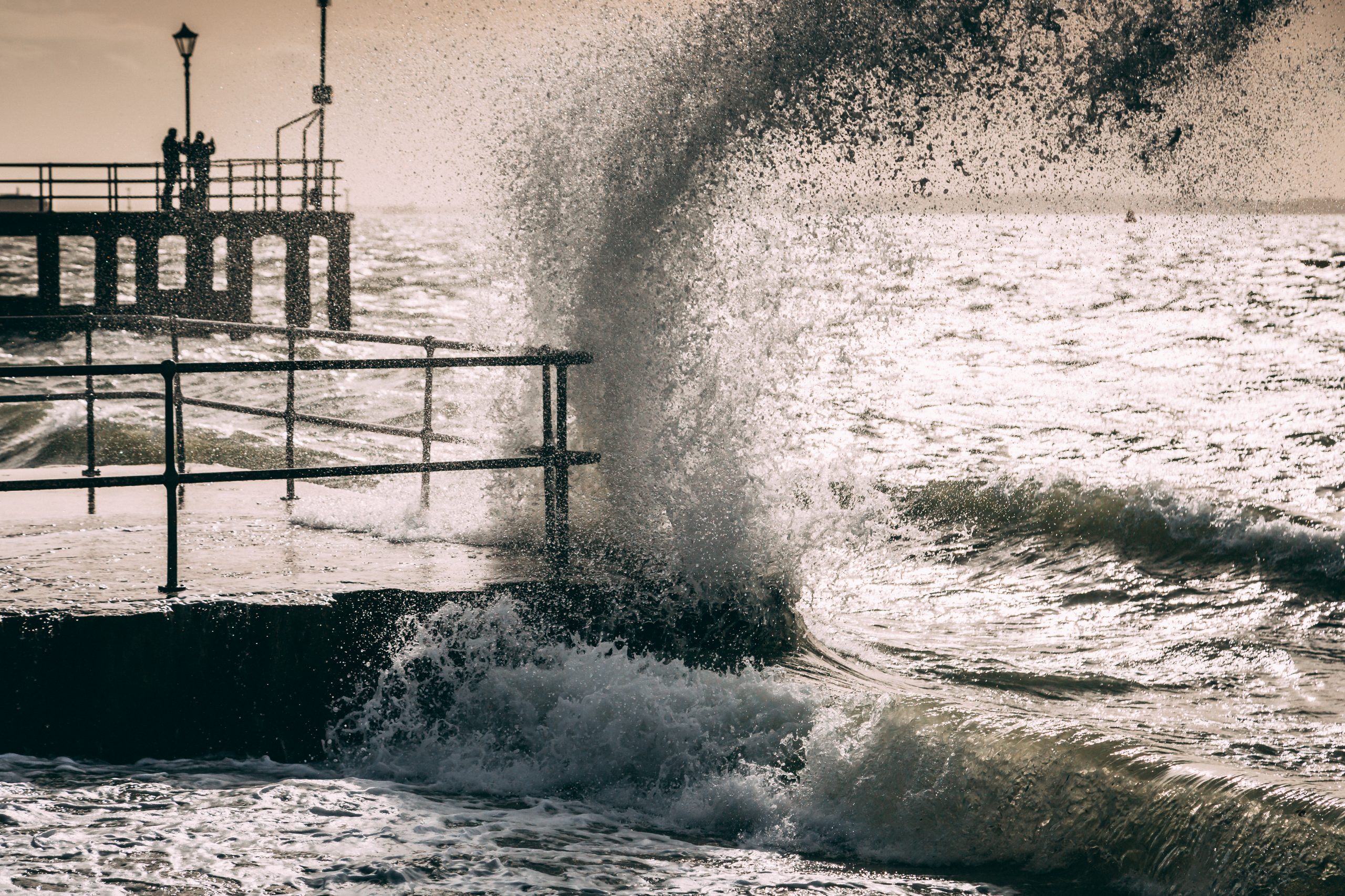 A wave of water reaches up in to the sky as it breaks against a wall